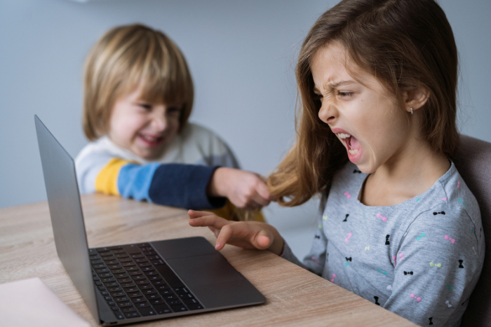 Two young children squabbling at a laptop, one pulling the other's hair