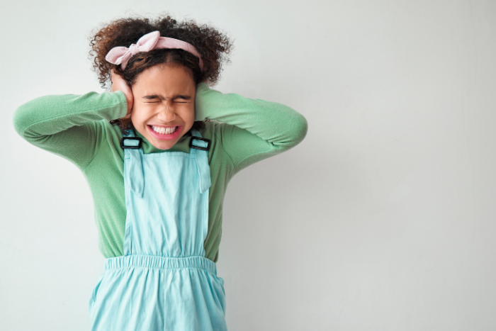 Young girl in mint overalls covering her ears with both hands, overwhelmed
